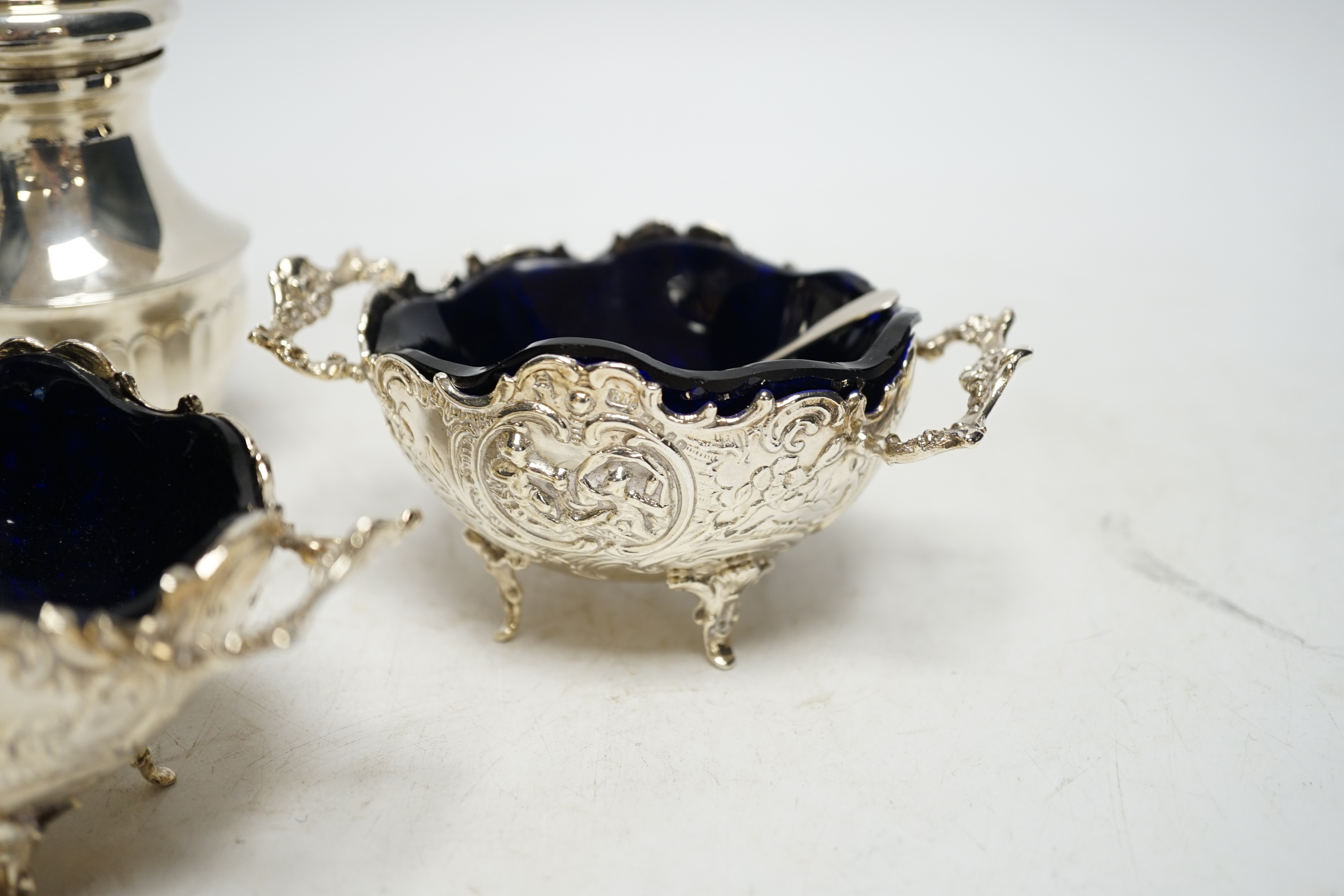 A pair of late 19th century Hanau silver two handled salts, with blue glass liners, import marks for Chester, 1899, with two associated spoons and two silver pepper mills. Condition - fair